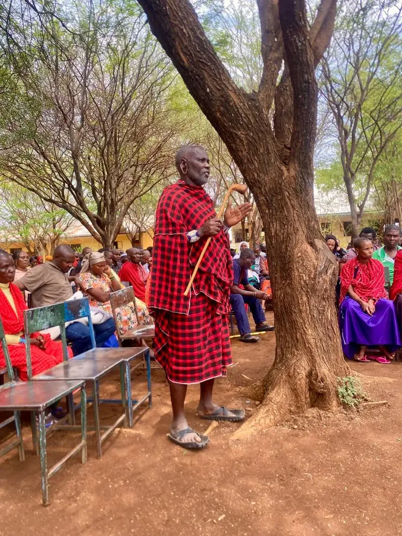 A Maasai elder addressing a community gathering under a tree