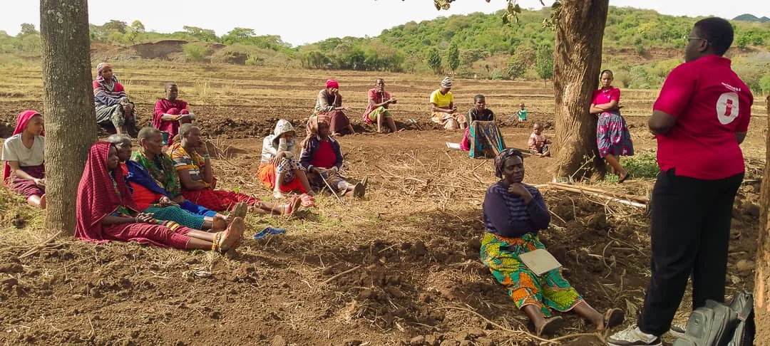 Villagers seated on open ground for a community health session