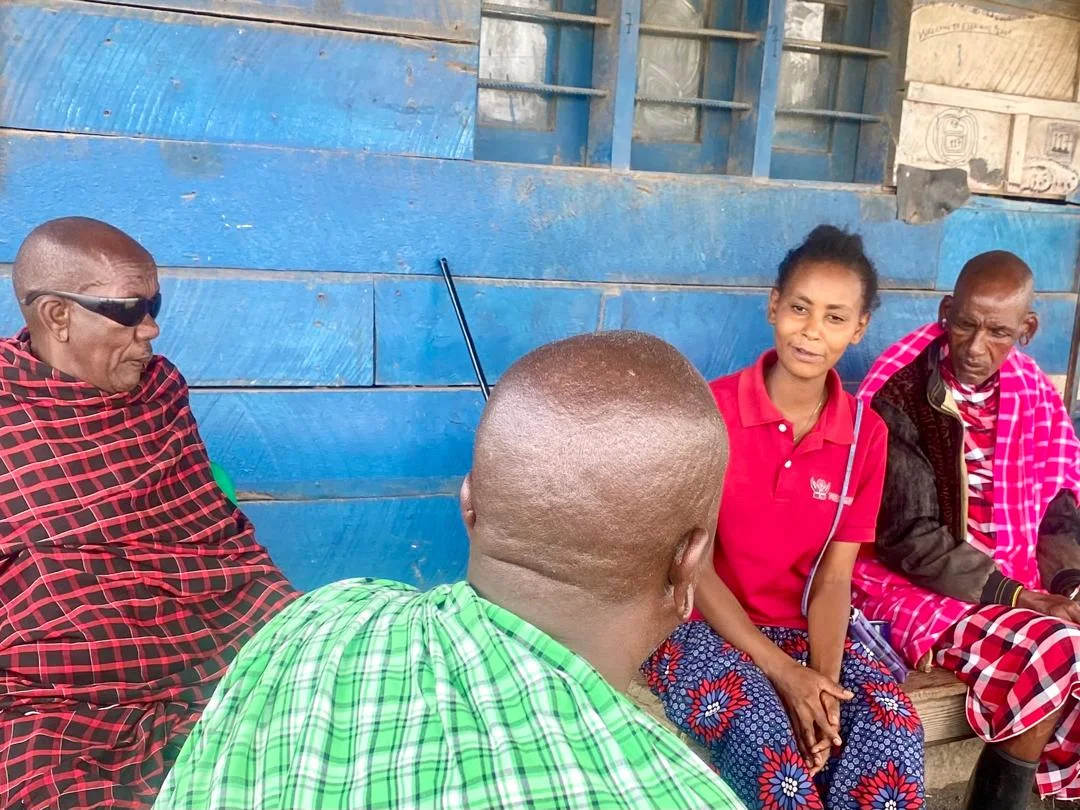 A health worker sitting with Maasai elders outside a rural clinic