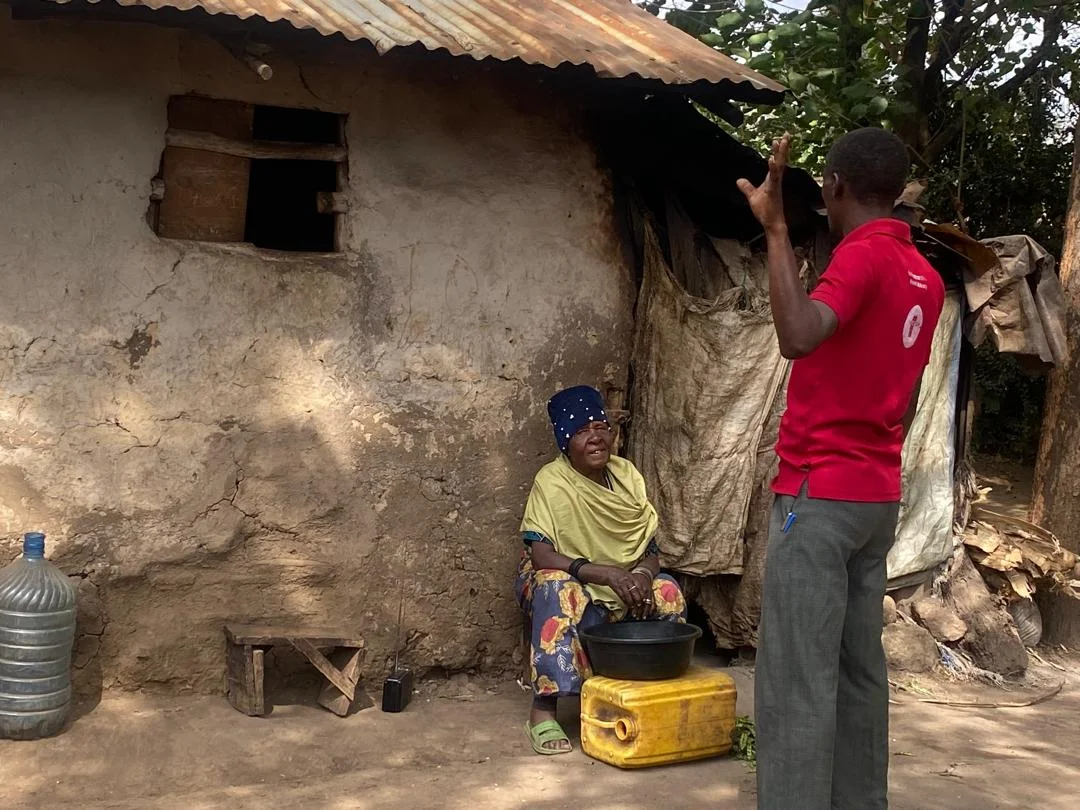 A health worker visiting an elderly woman outside her mud-walled home